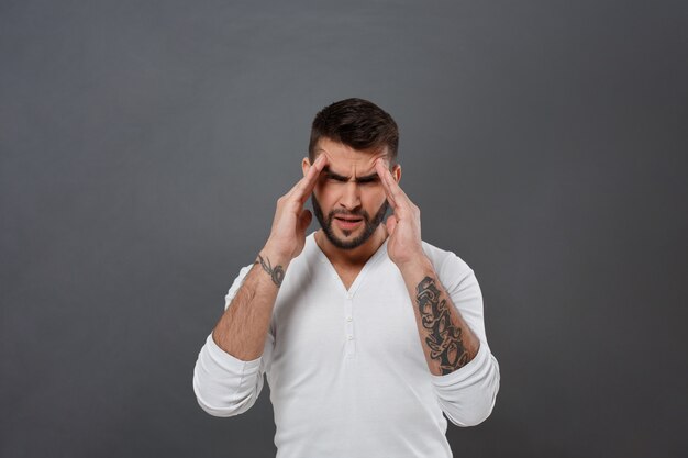 Il giovane uomo bello ha mal di testa sopra la parete grigia