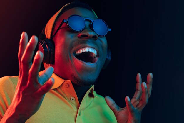 Il giovane uomo bello hipster felice ascoltando musica con le cuffie al nero con luci al neon