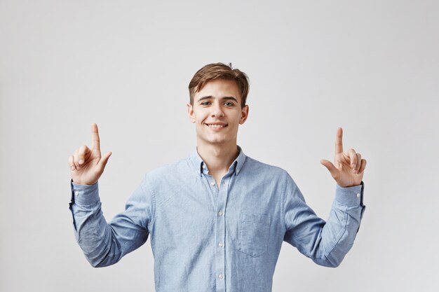 Il giovane uomo bello sta osservando in su, indicando le sue dita in su