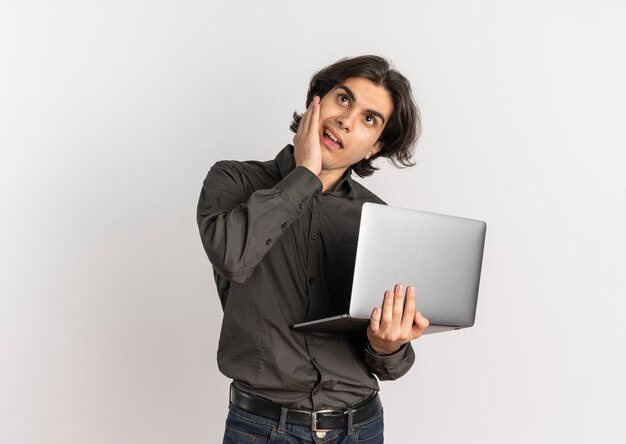 Il giovane uomo caucasico bello infastidito tiene il computer portatile e guarda in alto isolato su priorità bassa bianca con lo spazio della copia