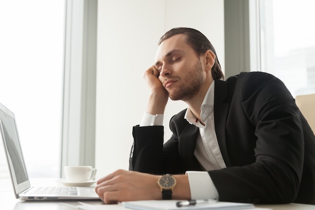 Il giovane uomo d&#39;affari ha dozzeggiato davanti al computer portatile sul lavoro.