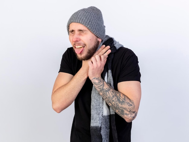 Il giovane uomo malato caucasico dolorante che indossa sciarpa e cappello invernale sporge la lingua e si soffoca