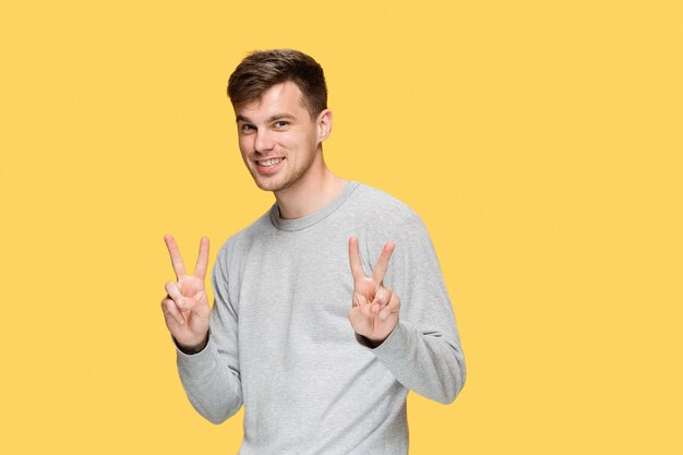 Il giovane uomo sorridente e guardando la telecamera su giallo studio