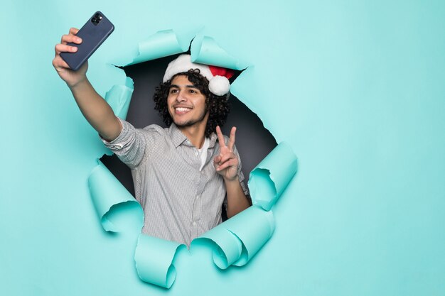 Il giovane usura bella riccia dell'uomo in cappello di Santa prende il selfie dal foro su Libro Verde