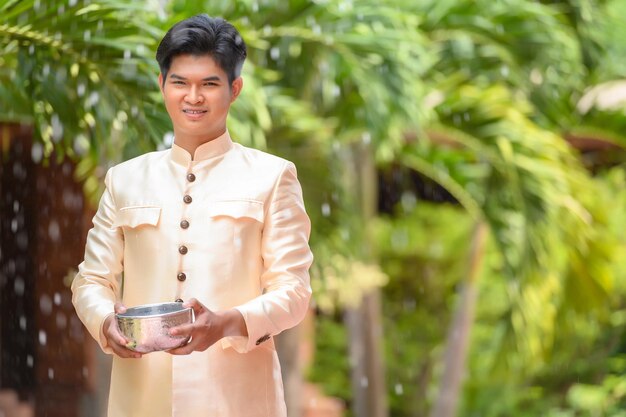 Il giovane vestito con splendidi costumi tailandesi si diverte a spruzzare acqua dalla ciotola nel tempio e preserva la buona cultura del popolo tailandese durante il festival di Songkran, il giorno della famiglia di Capodanno tailandese ad aprile