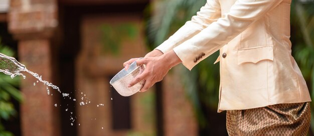 Il giovane vestito con splendidi costumi tailandesi si diverte a spruzzare acqua dalla ciotola nel tempio e preserva la buona cultura del popolo tailandese durante il festival di Songkran, il giorno della famiglia di Capodanno tailandese ad aprile