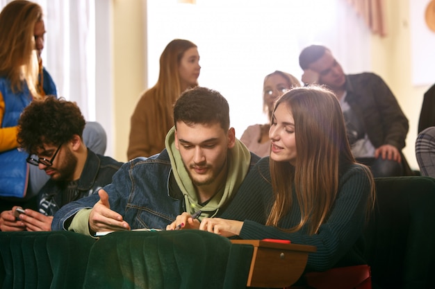 Il gruppo di allegri studenti felici seduti in un'aula prima della lezione