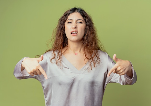 Il lavoratore di ufficio femminile grazioso giovane dispiaciuto indica giù isolato sulla parete verde oliva