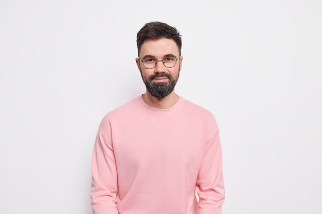 Il macho barbuto fiducioso sembra contento, ha un sorriso gentile amichevole sul viso indossa occhiali rotondi maglione rosa pink