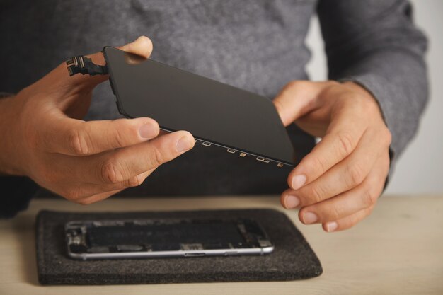 Il maestro tiene un nuovo schermo per la sostituzione sopra lo smartphone smontato nel suo laboratorio, da vicino