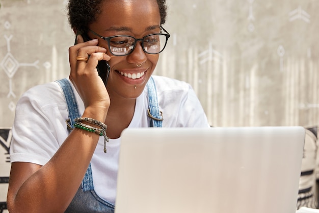 Il manager di successo della giovane donna felice chiama tramite smart phone mentre lavora sul computer portatile