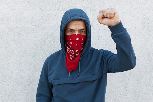 Il manifestante con la maschera di bandana rossa alza il pugno