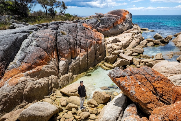Il maschio asiatico sta posando per la telecamera mentre si trova su grandi rocce vicino a un mare