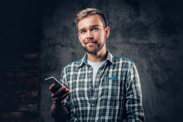 Il maschio hipster barbuto in una maglietta in pile tiene lo smartphone su sfondo grigio.