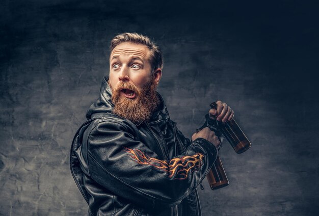 Il maschio hipster ubriaco con la barba rossa emotiva e divertente tiene birra artigianale in bottiglia.