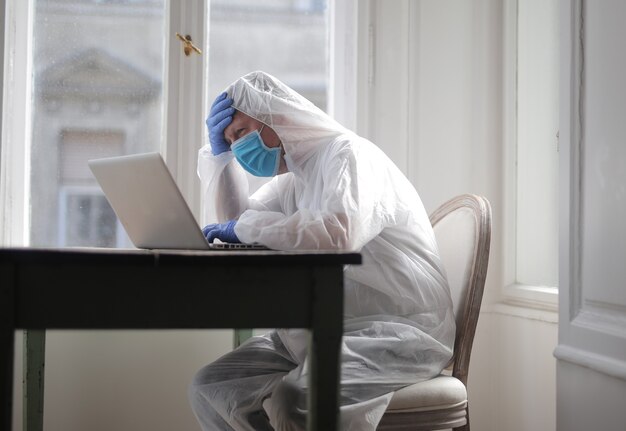 Il maschio lavora su un computer protetto da tuta medica e maschera