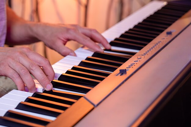 Il maschio passa sui tasti di un pianoforte su un bellissimo sfondo colorato da vicino.