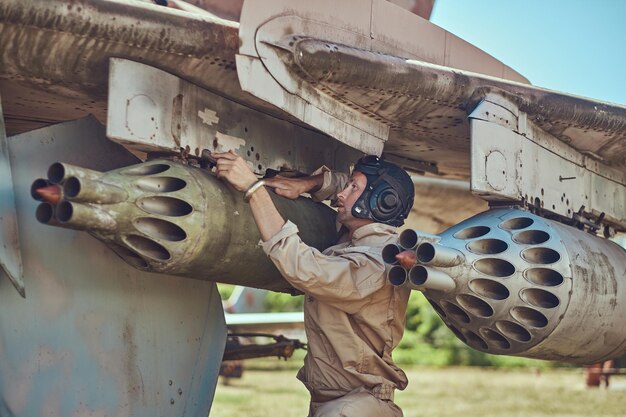 Il meccanico in uniforme e il casco volante riparano il vecchio caccia-intercettore di guerra in un museo all'aperto.