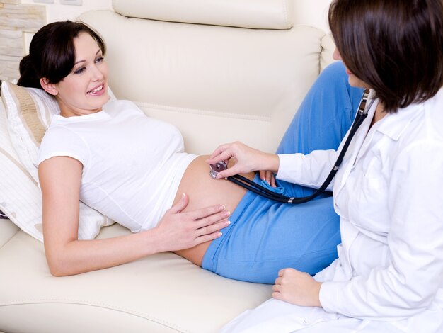 Il medico femminile ascolta la pancia di una donna incinta
