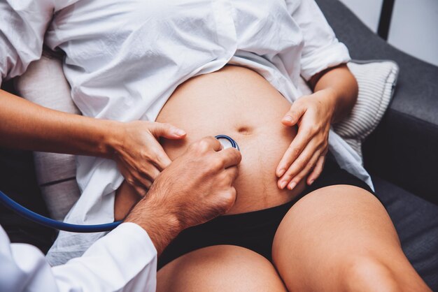 Il medico sta controllando la donna incinta con lo stetoscopio nel concetto di assistenza sanitaria dell'ospedale