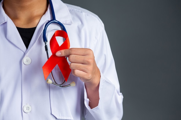 Il medico tiene in mano un nastro rosso, la consapevolezza dell'HIV, la Giornata mondiale contro l'AIDS e la Giornata mondiale della salute sessuale.