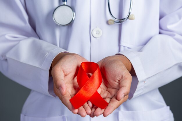 Il medico tiene in mano un nastro rosso, la consapevolezza dell'HIV, la Giornata mondiale contro l'AIDS e la Giornata mondiale della salute sessuale.
