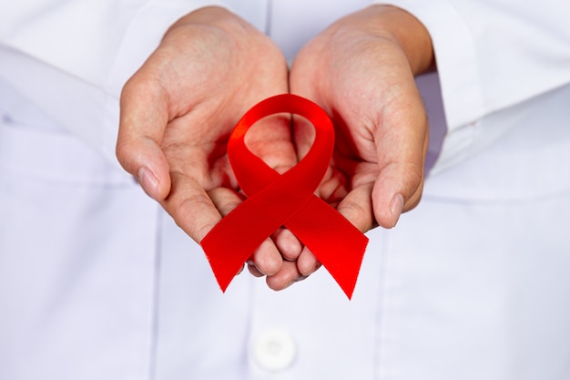 Il medico tiene in mano un nastro rosso, la consapevolezza dell'HIV, la Giornata mondiale contro l'AIDS e la Giornata mondiale della salute sessuale.