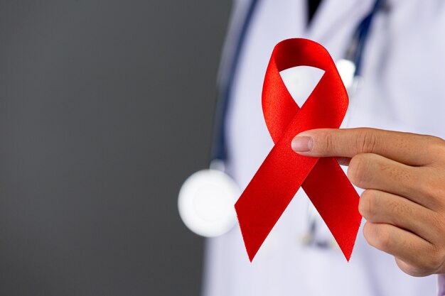 Il medico tiene in mano un nastro rosso, la consapevolezza dell'HIV, la Giornata mondiale contro l'AIDS e la Giornata mondiale della salute sessuale.