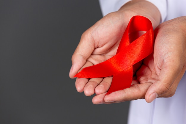 Il medico tiene in mano un nastro rosso, la consapevolezza dell'HIV, la Giornata mondiale contro l'AIDS e la Giornata mondiale della salute sessuale.