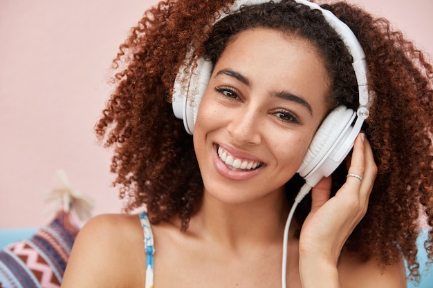 Il melomano femminile afroamericano dalla pelle scura positiva ascolta musica popolare online, ha un ampio sorriso