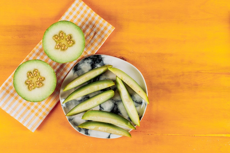 Foto gratuito il melone si sbuccia in un piatto bianco con diviso nella vista superiore del mezzo melone su un fondo arancio