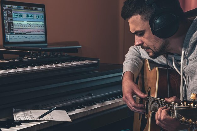 Il musicista maschio suona la chitarra a casa sul posto di lavoro vicino al computer