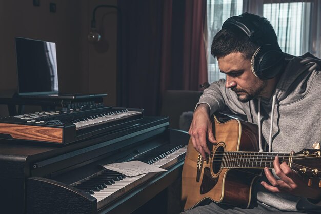 Il musicista maschio suona la chitarra a casa sul posto di lavoro vicino al computer