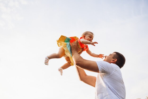 Il padre felice tiene la bambina affascinante su sotto il cielo dell&#39;estate