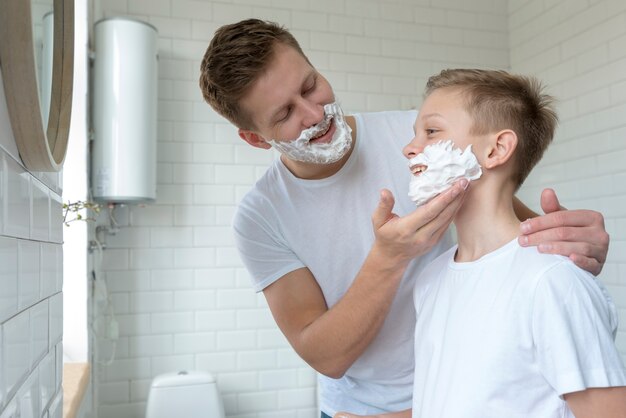 Il padre mette la crema da barba sul viso del figlio