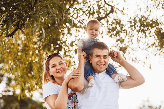 Il papà felice della mamma tiene la piccola figlia sulle loro armi che stanno nei raggi del sole di sera