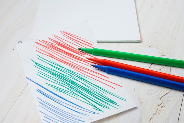 Il pennarello colorato e la carta con il colpo di penna sulla tavola di legno bianca