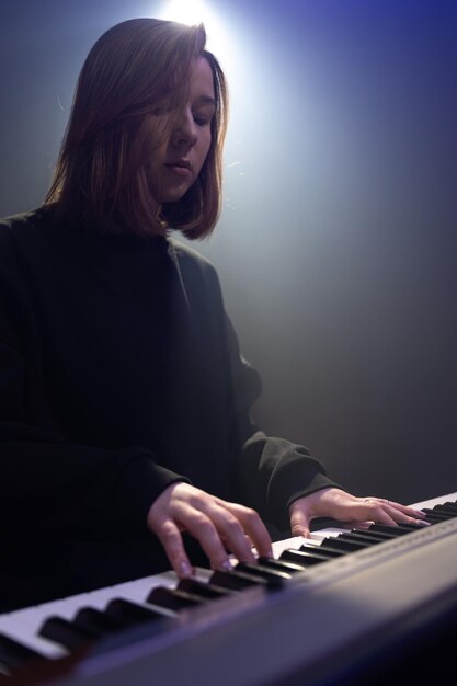 Il pianista della giovane donna suona i tasti in una stanza buia con foschia