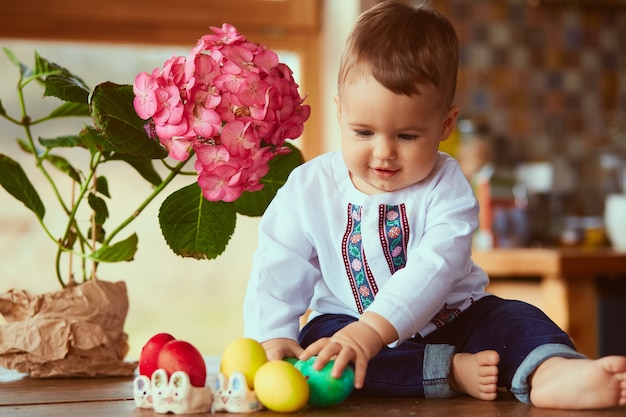 Il piccolo bambino si siede vicino alle uova di Pasqua