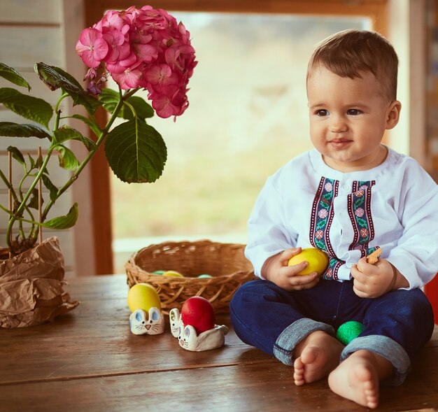 Il piccolo bambino tiene un uovo giallo e si siede sul tavolo