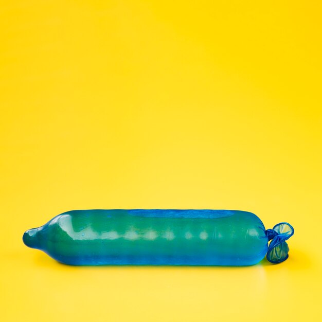 Il preservativo blu scuro ha riempito di acqua su fondo giallo