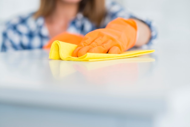 Il primo piano dei guanti d&#39;uso della donna pulisce lo scrittorio bianco con il tovagliolo giallo