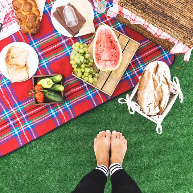 Il primo piano dei piedi della donna vicino allo spuntino di picnic su coperta
