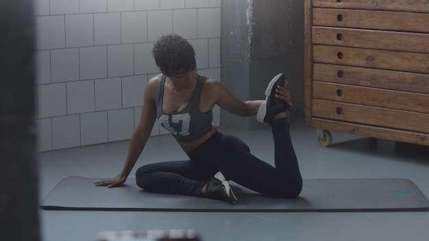 Il primo piano della donna afroamericana di razza mista fa una routine di allungamento sul pavimento in un loft soleggiato Gambe che si allungano