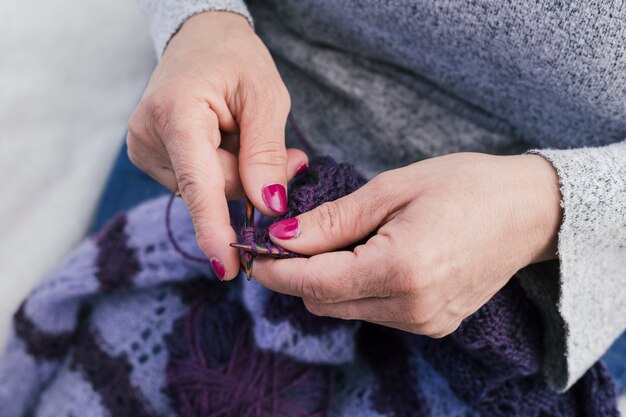 Il primo piano della donna lavora a maglia i vestiti di lana con i ferri da maglia