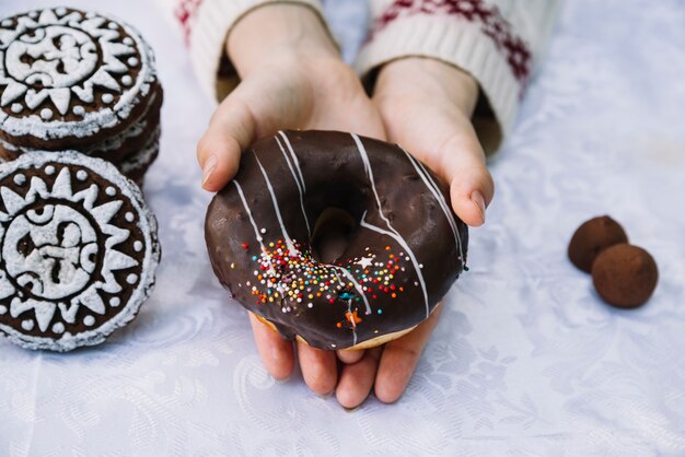 Il primo piano delle mani che tengono la ciambella del cioccolato con spruzza