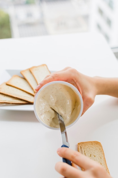 Il primo piano di una femmina che prende il formaggio si è sparso con il coltello per applicarlo sul pane sopra la tavola