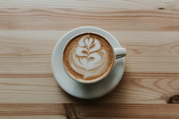 Il primo piano ha sparato di caffè con arte del latte in tazza da the ceramico bianco su una tavola di legno