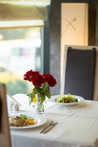 Il primo piano selettivo verticale ha sparato le rose rosse sulla tavola vicino ai piatti riempiti di alimento sulla tavola