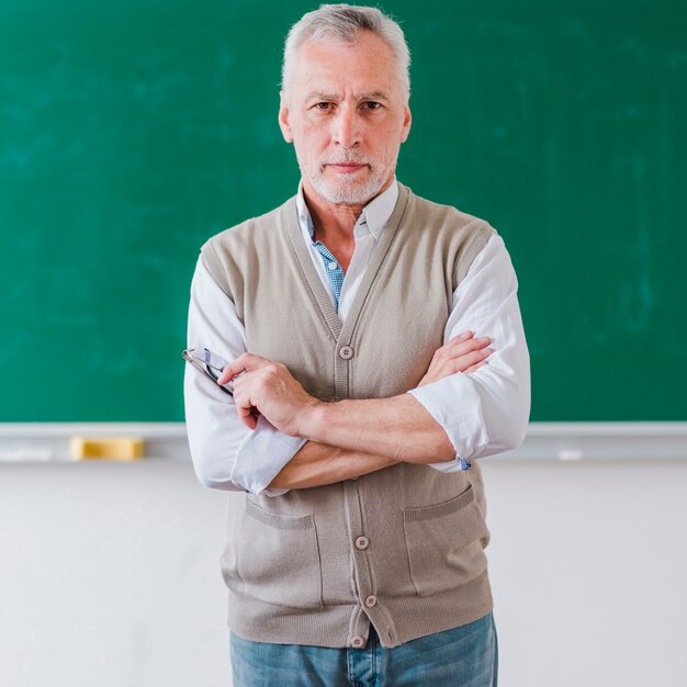 Il professore maschio senior con le armi ha attraversato la condizione contro la lavagna